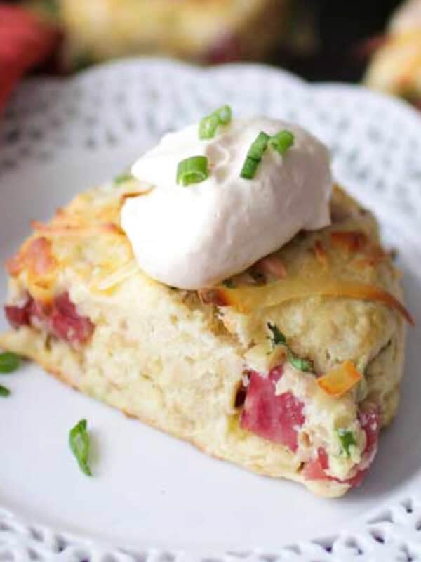 a ham and cheese scone topped with horseradish cream on a white plate.