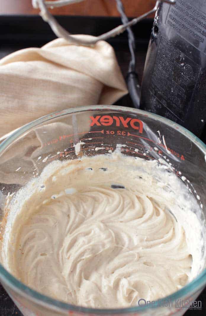 Whipping together cream cheese and heavy cream in a glass bowl.
