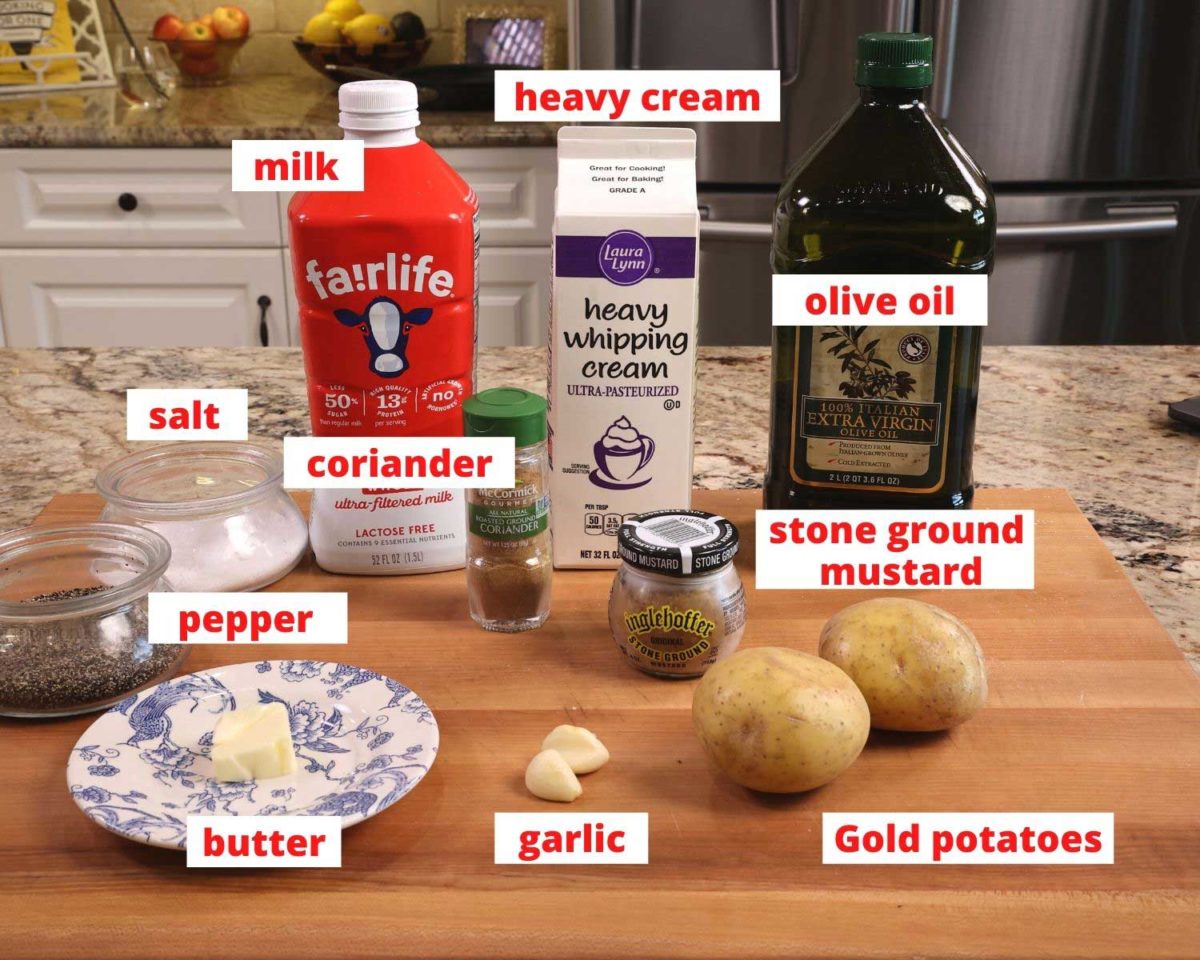 ingredients needed to make mashed potatoes on a wooden cutting board: potatoes, milk, cream, mustard, and butter