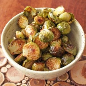a green bowl filled with roasted brussels sprouts on a wooden table.