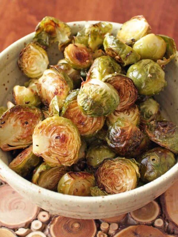 a green bowl filled with roasted brussels sprouts on a wooden table.