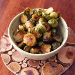 a green bowl filled with roasted brussels sprouts on a wooden table