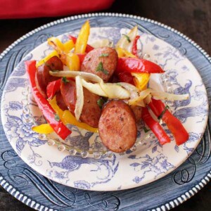 Roasted sausage, red and yellow peppers and onions in a white and blue bowl