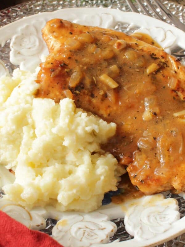 a single pan seared turkey cutlet with gravy next to mashed potatoes on a white plate.