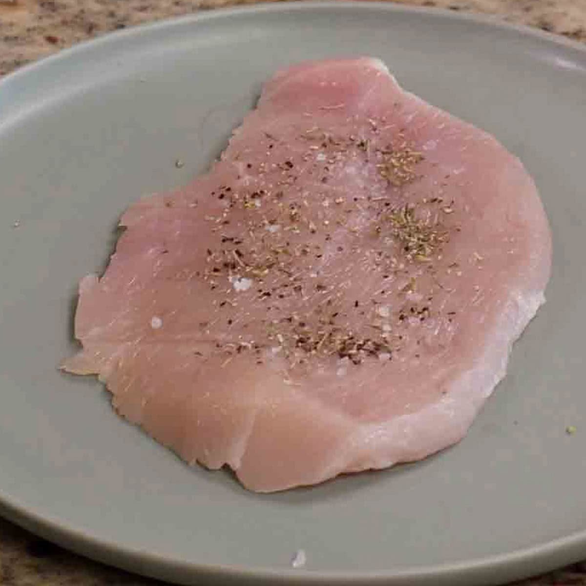 a turkey cutlet seasoned with italian seasoning on a green plate.