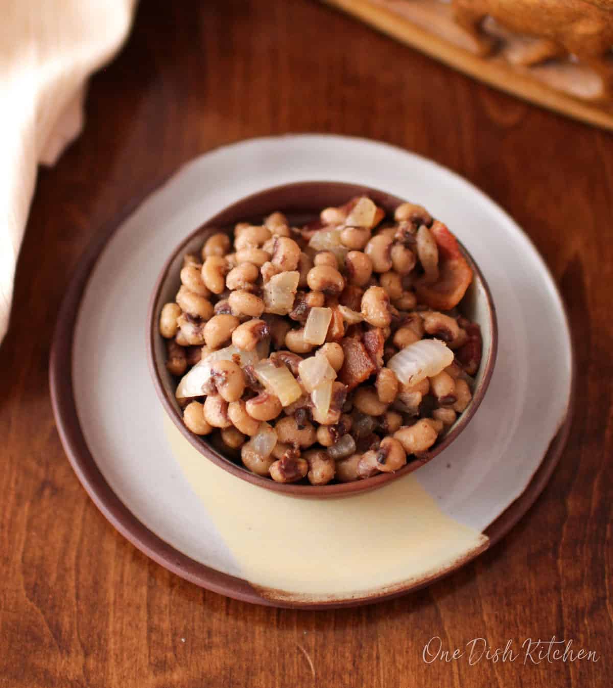 a bowl of black eyed peas on a wooden table next to a brown napkin.