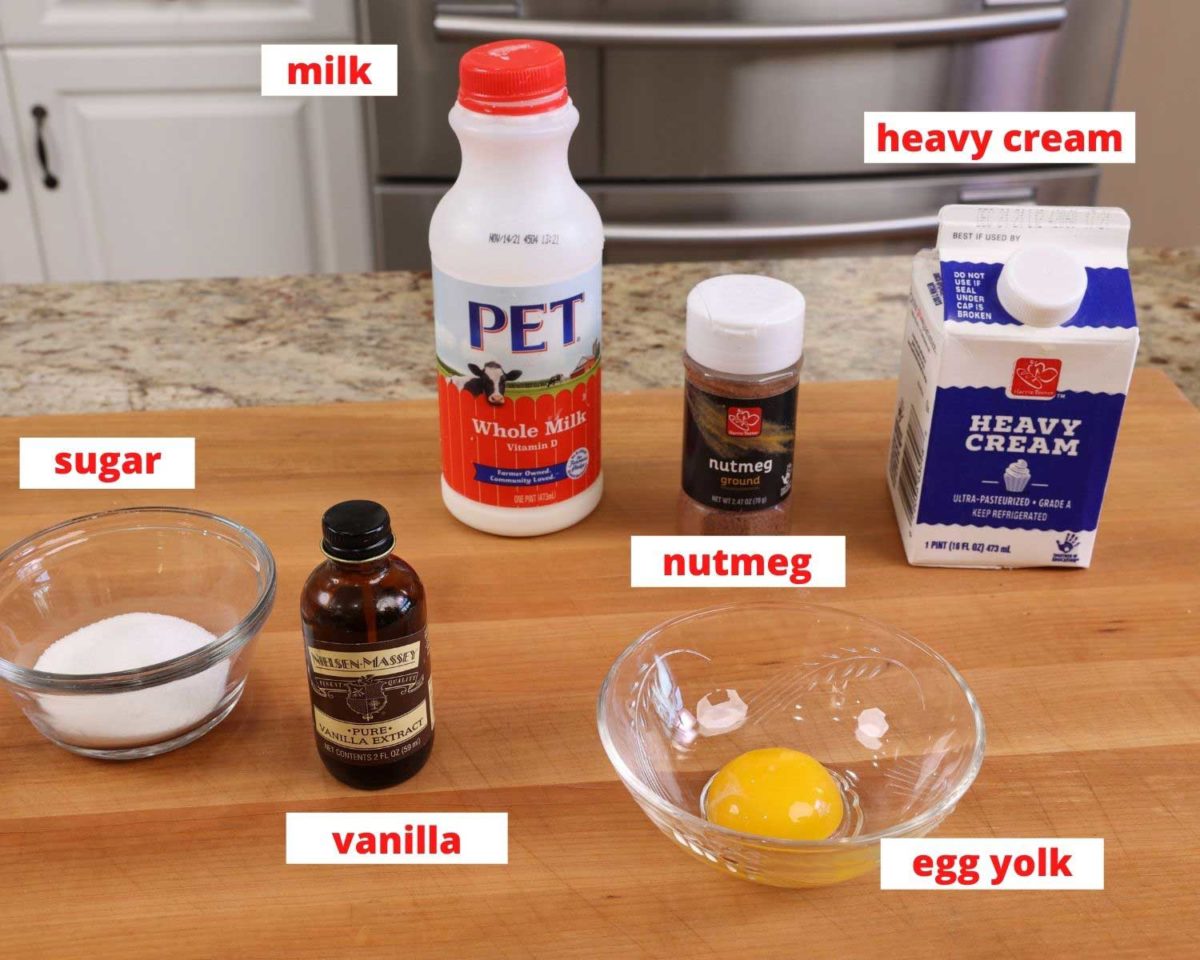 milk, cream, egg, vanilla, and nutmeg on a wooden cutting board.