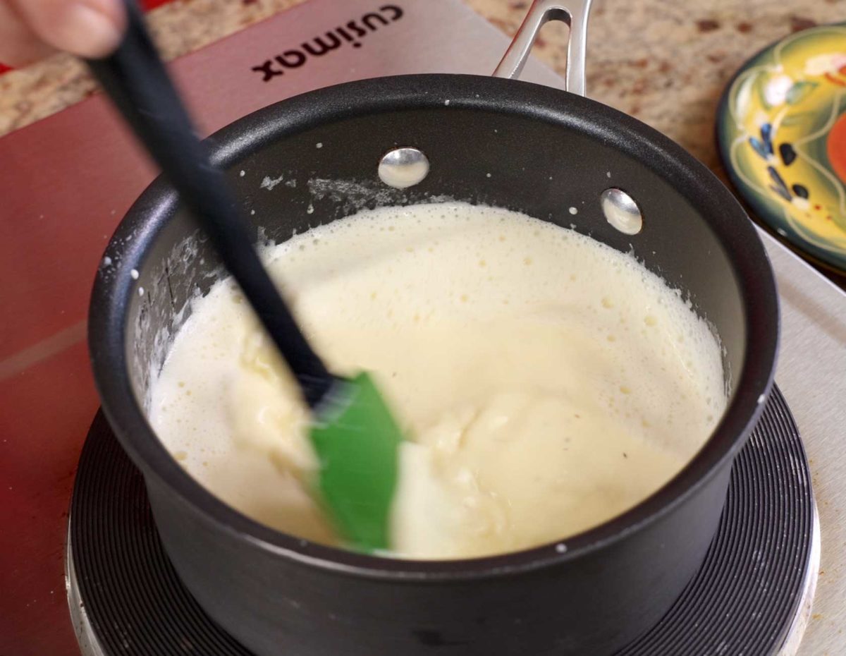 whisking homemade eggnog in a small black saucepan.