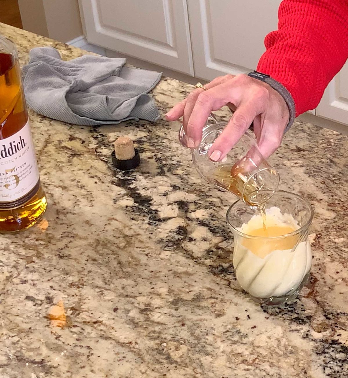 pouring whiskey into a glass of eggnog.