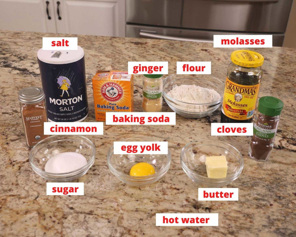 flour, spices, molasses, an egg, and other ingredients needed to make gingerbread on a wooden cutting board.
