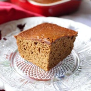 A square slice of gingerbread on a small plate with the baking dish in the background