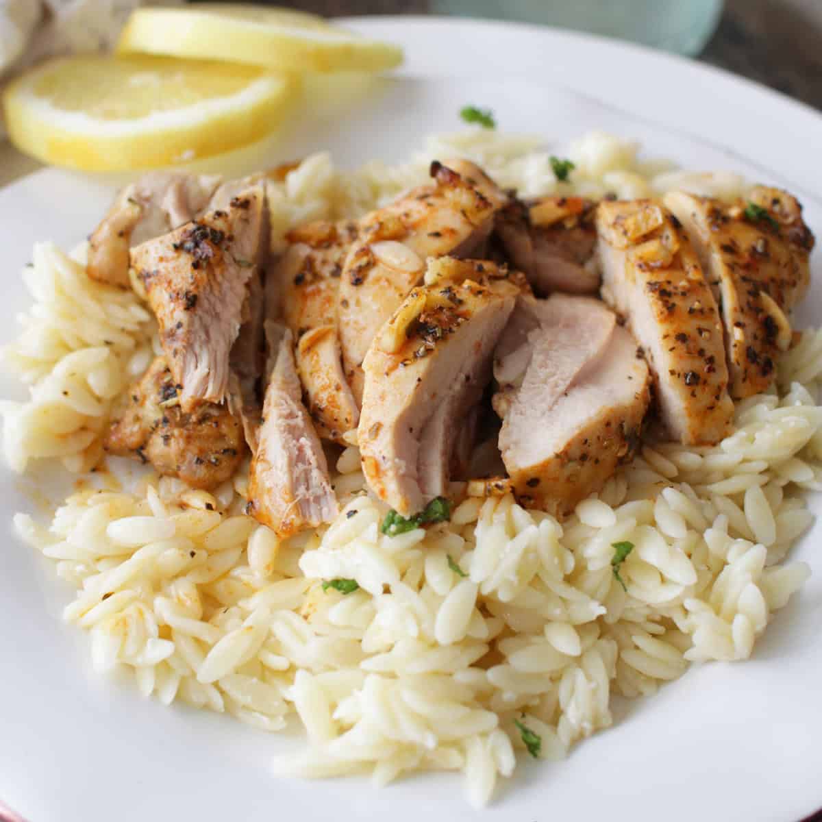 Sliced chicken over orzo pasta on a plate with two lemon wheels.