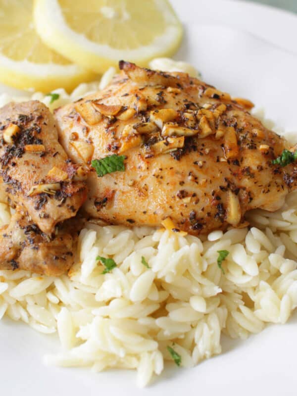 two baked chicken thighs over orzo pasta next to slices of lemon.