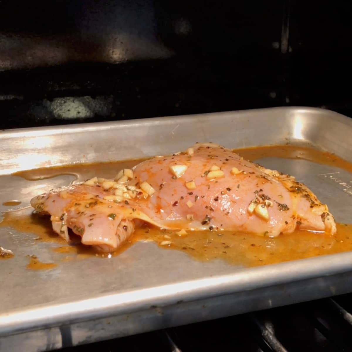 one chicken breast topped with garlic on a baking sheet in an oven