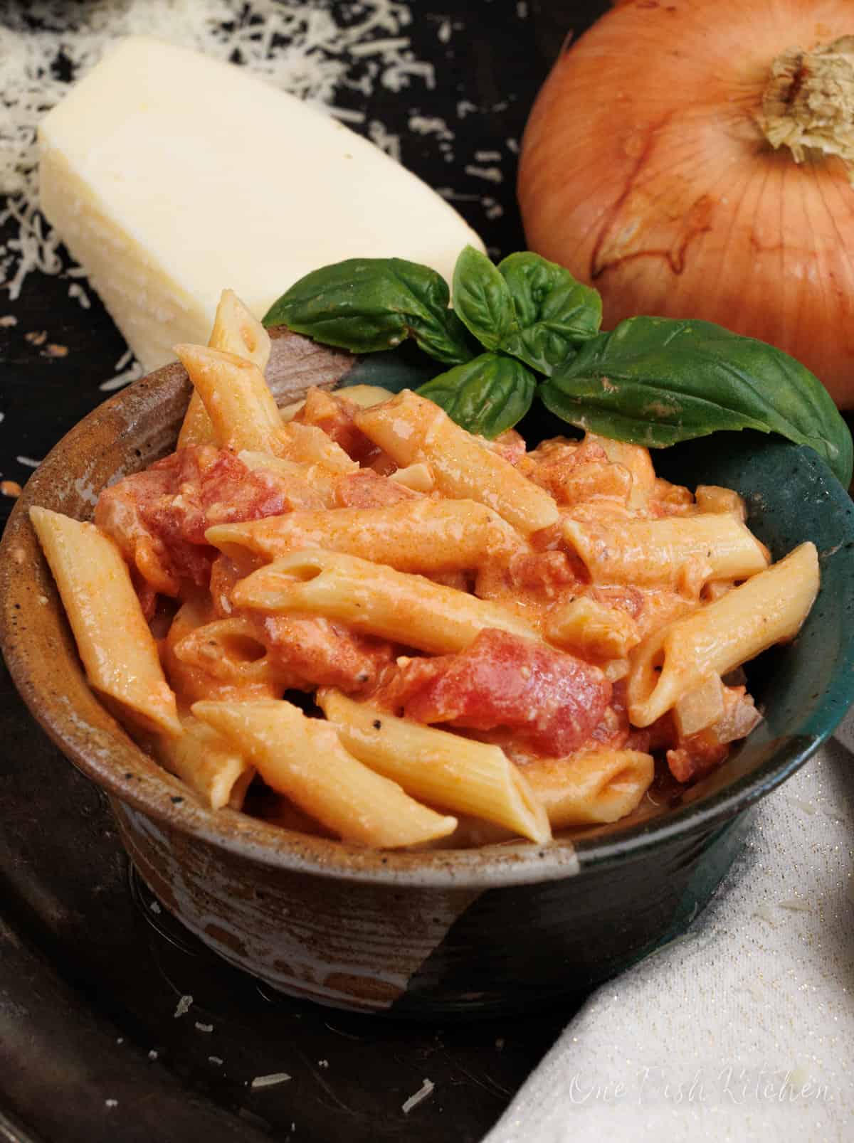 a green bowl filled with penne pasta topped with vodka sauce next to an onion and a wedge of parmesan cheese