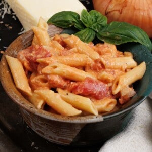 a green bowl filled with penne pasta topped with vodka sauce next to an onion and a wedge of parmesan cheese