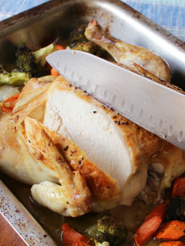 a whole chicken roasted on a bed of vegetables in a baking pan.