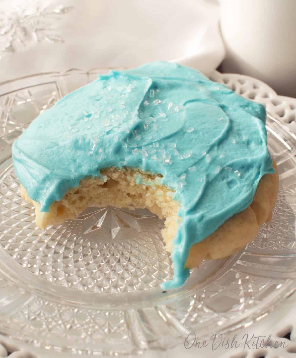 A bite missing from a blue frosted sugar cookie with white crystal sprinkles on a small plate