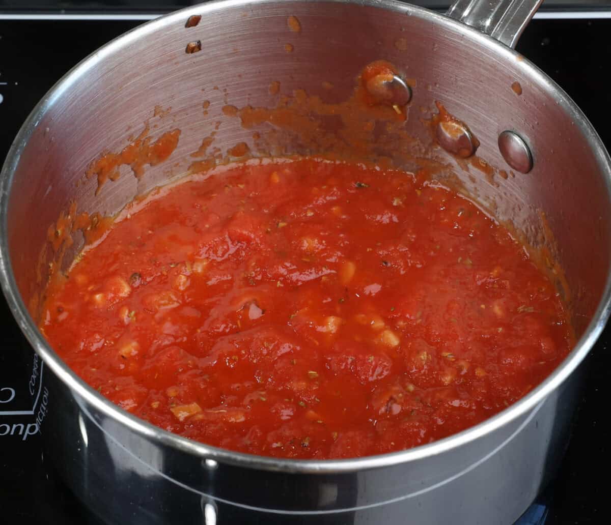 a small batch of homemade tomato sauce with canned tomatoes simmering in a pot on the stove.