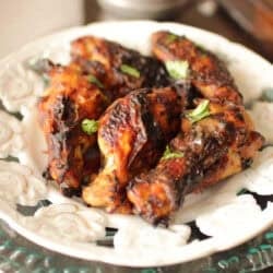 a plate of chicken wings next to a silver container filled with barbecue sauce.