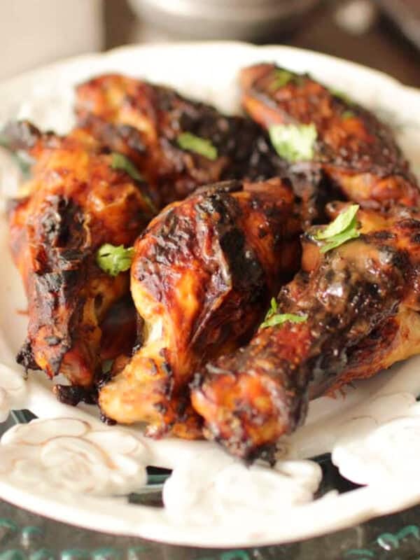 a plate of chicken wings next to a silver container filled with barbecue sauce.