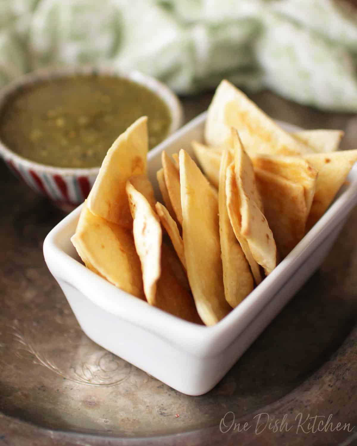 a single serving of homemade baked flour tortilla chips in a bowl next to salsa.