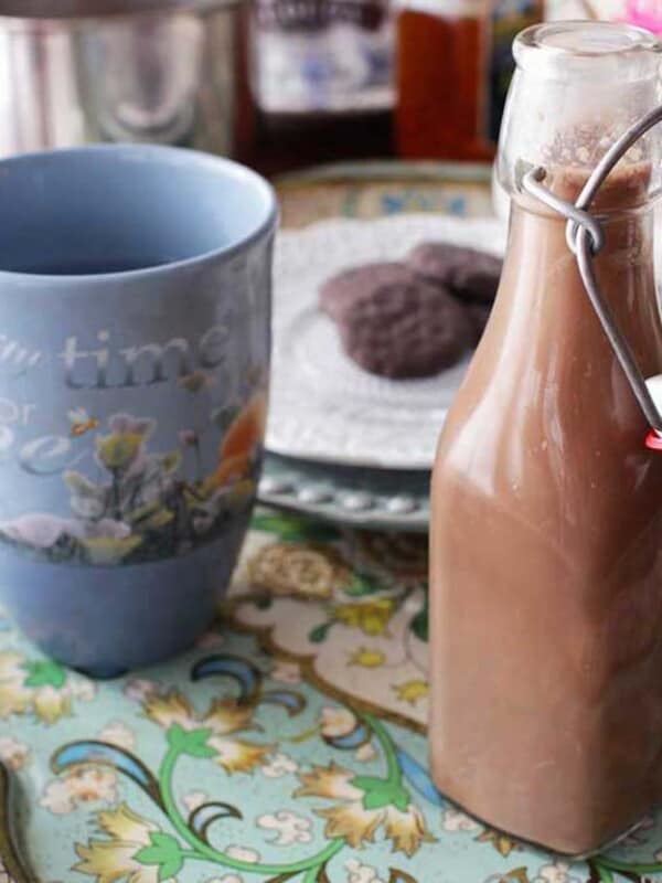 coffee creamer next to a blue coffee mug and a plate of cookies