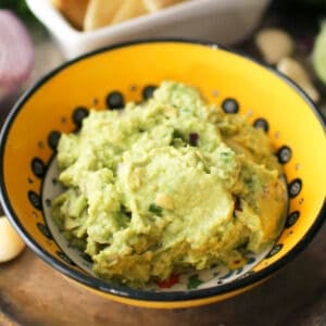 a bowl of guacamole next to a plate of chips.