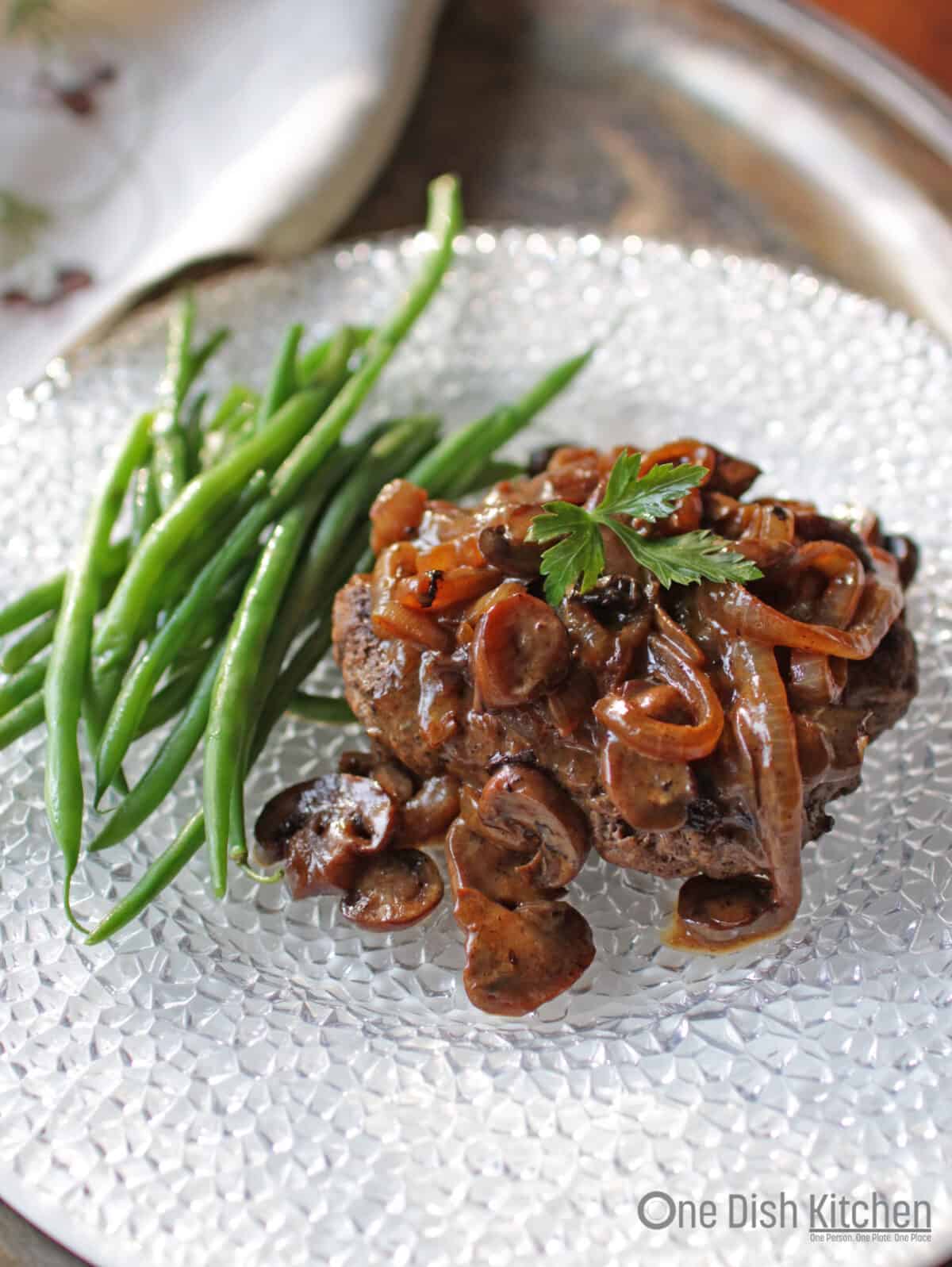 Salisbury Steak on a plate with green beans.