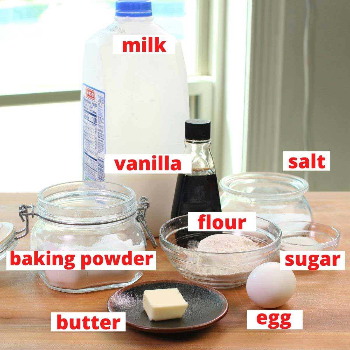 the ingredients needed for making waffles labeled and on a brown table.