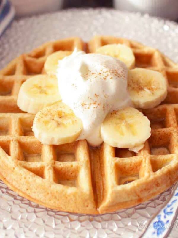 a waffle on a plate with sliced bananas and whipped cream.