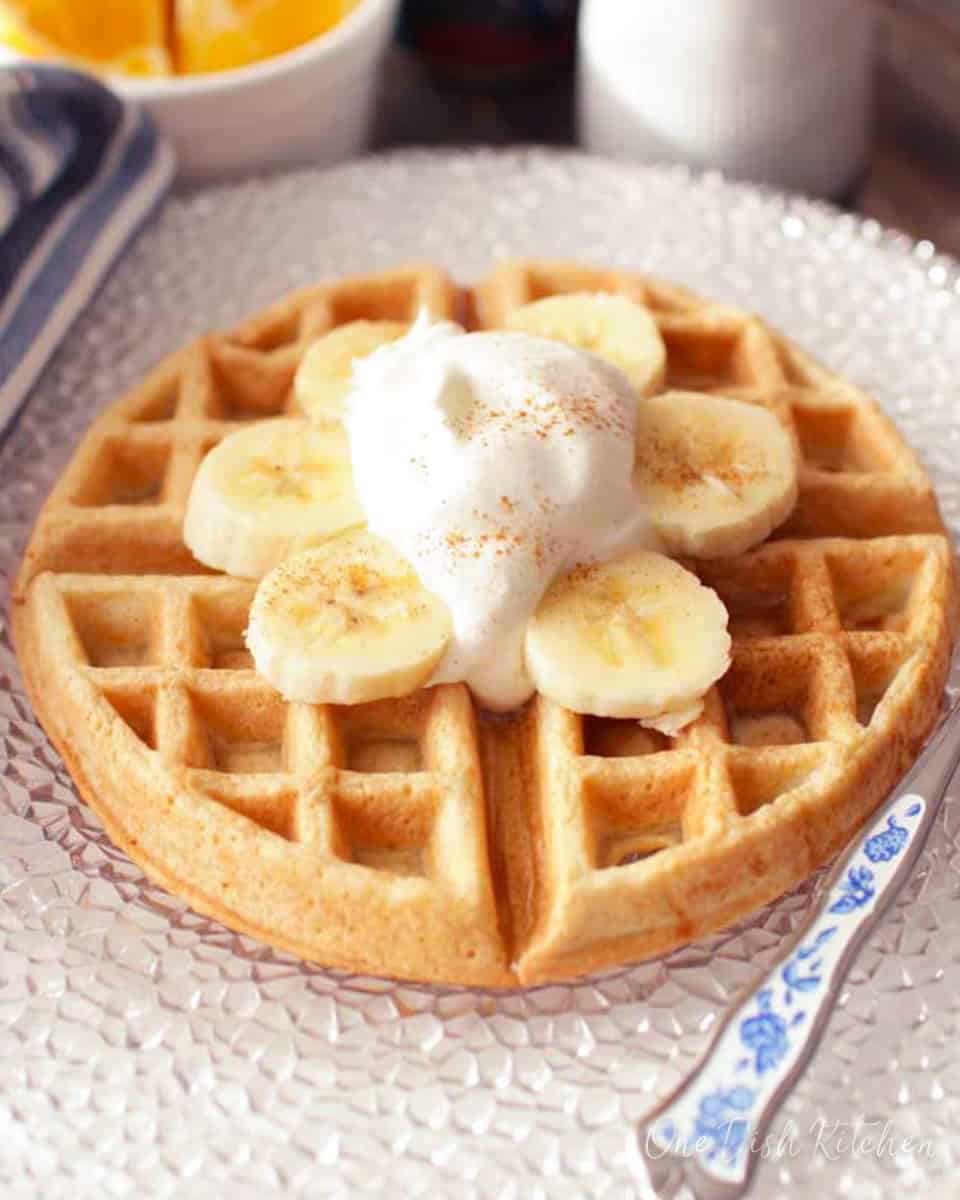 a waffle on a plate with sliced bananas and whipped cream.