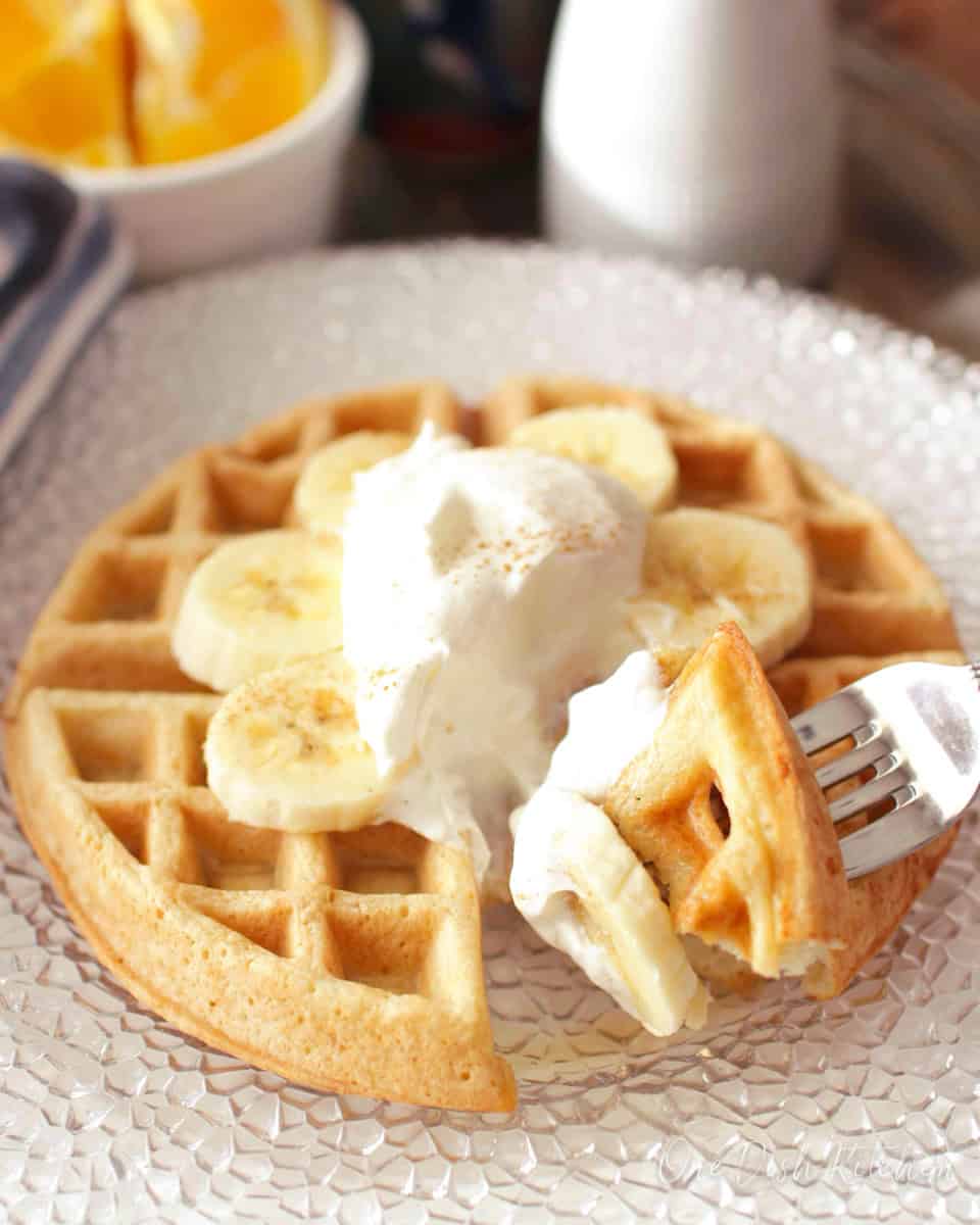 a single waffle topped with whipped cream and sliced bananas with a fork on the side.