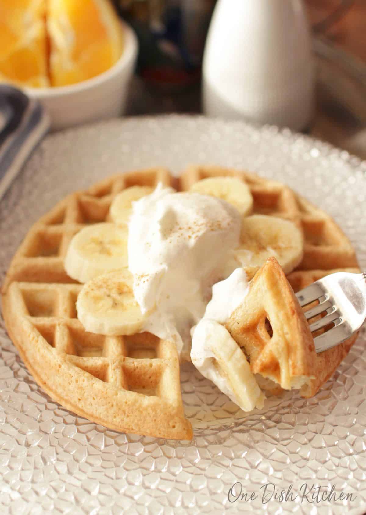 A forkful of waffle with whipped cream, banana slices, and dusted with cinnamon on a large plate.