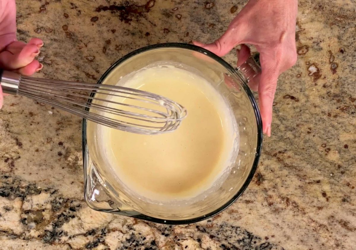 waffle batter in a mixing bowl with a whisk perched on the side of the bowl.