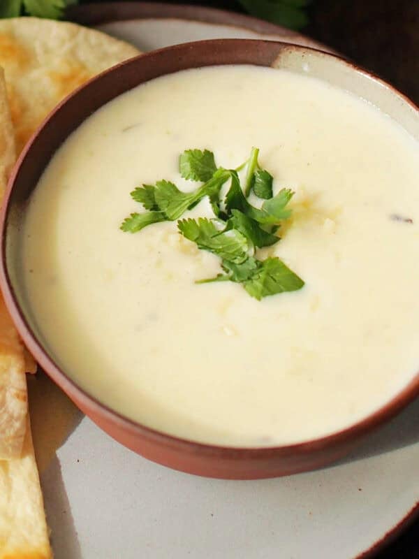 a small batch of white queso next to a plate of tortilla chips.