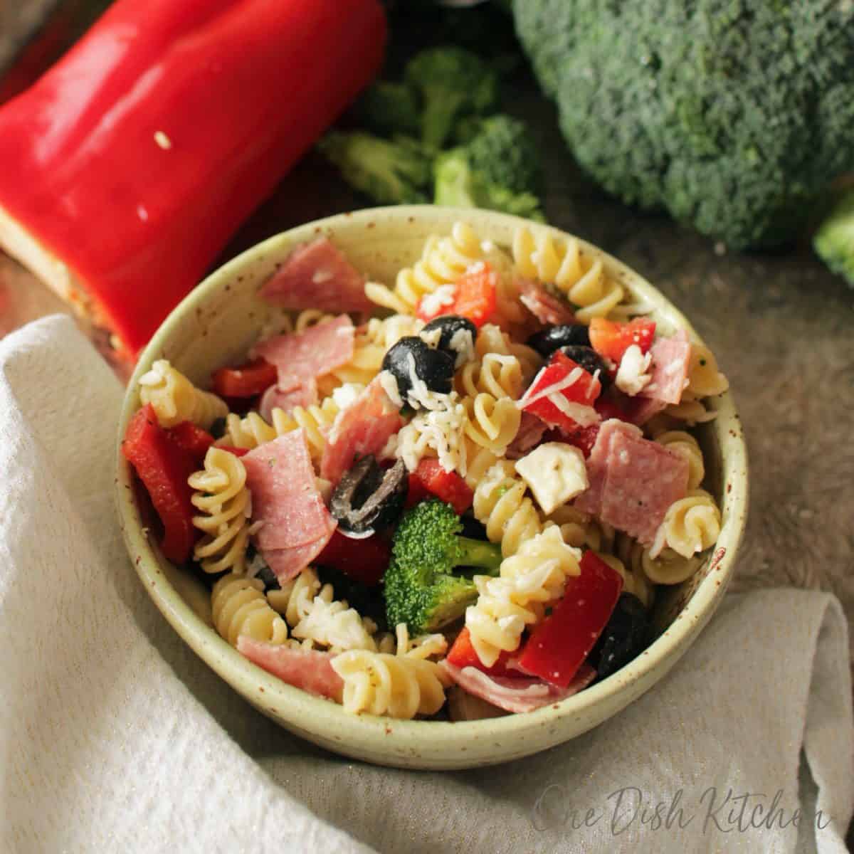 an overhead view of a bowl of pasta salad surrounded by fresh vegetables on a tray.