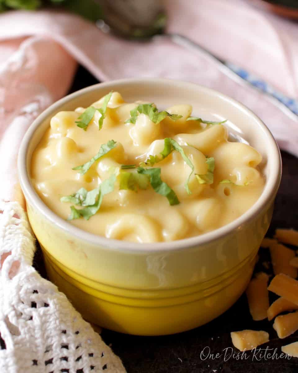 a small yellow bowl filled with macaroni and cheese next to a pink napkin.