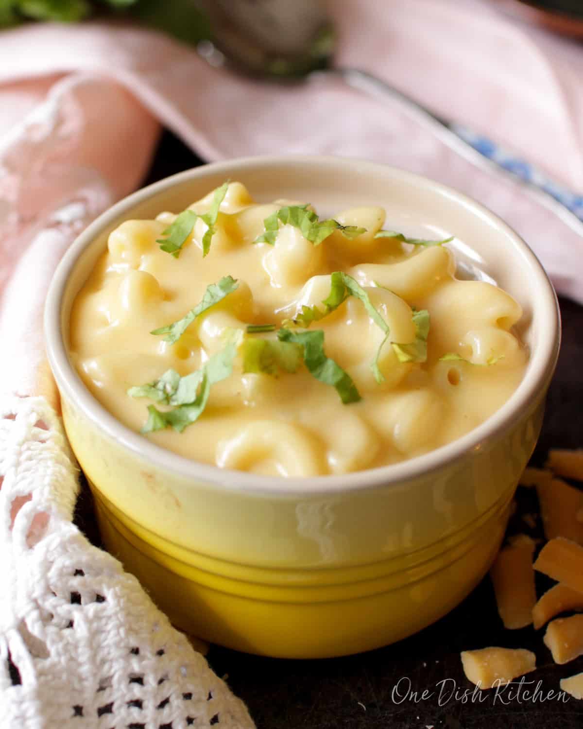 a small yellow bowl filled with macaroni and cheese next to a pink napkin.