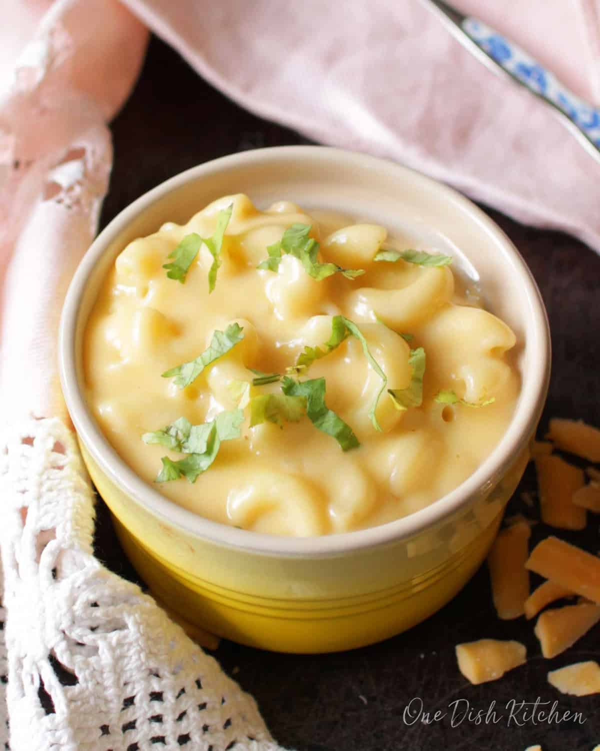a small yellow bowl filled with macaroni and cheese next to a pink napkin.