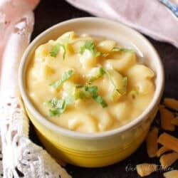 a small yellow bowl filled with macaroni and cheese next to a pink napkin.