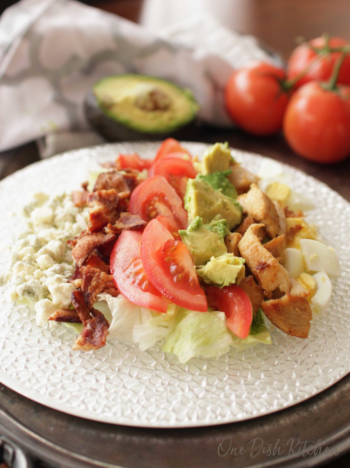 a plate filled with lettuce, tomatoes, blue cheese, avocados, and crumbled bacon