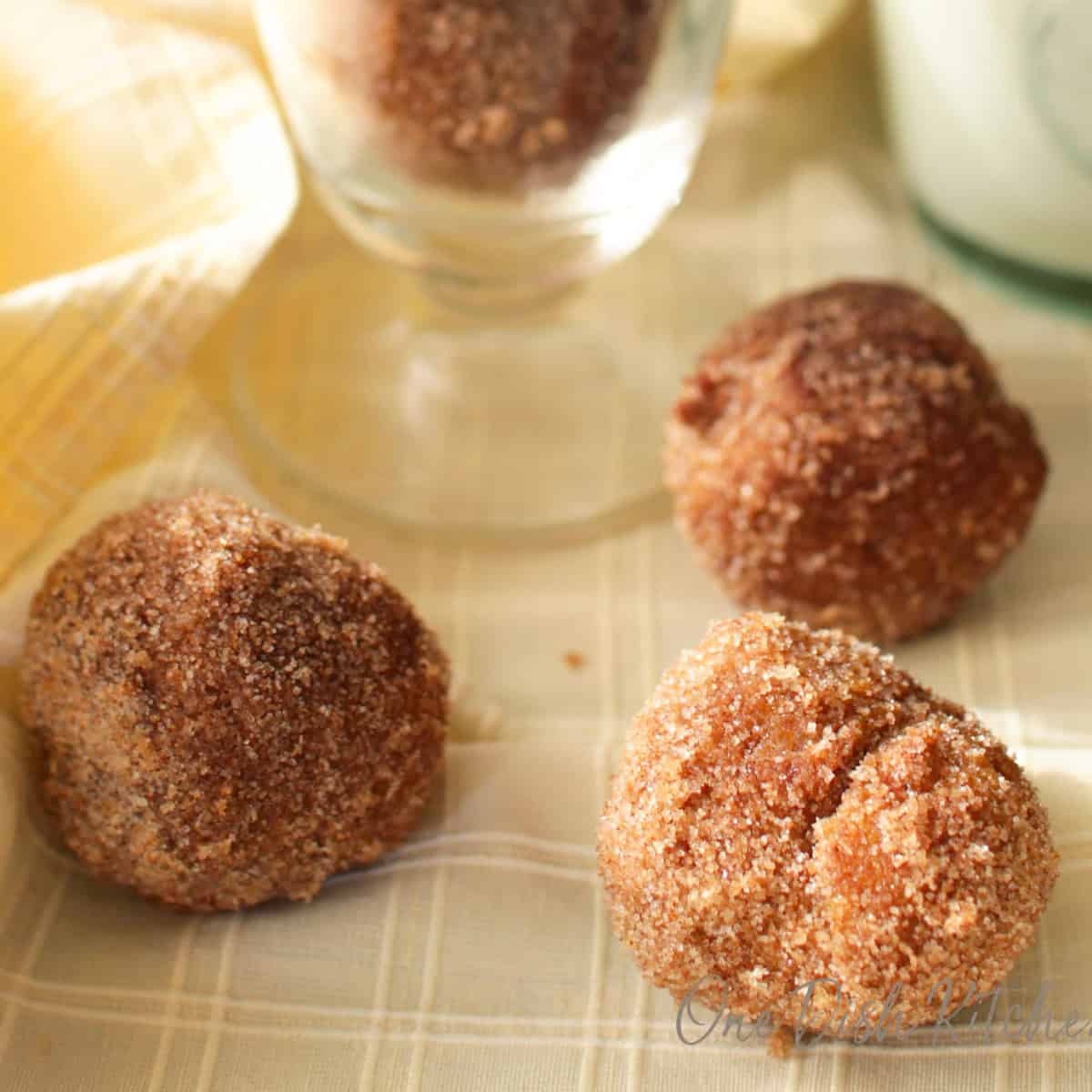 three fried donut holes with a cinnamon sugar coating on a yellow napkin.