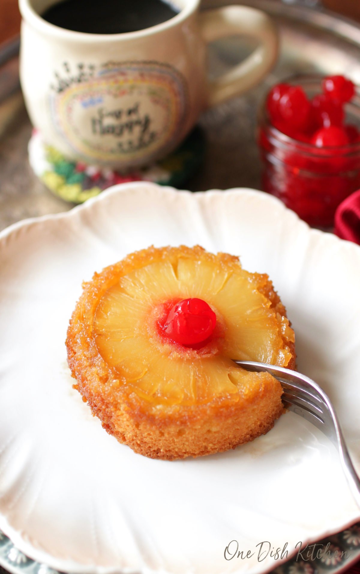 a mini pineapple upside down cake on a white plate with a fork cutting into the cake.