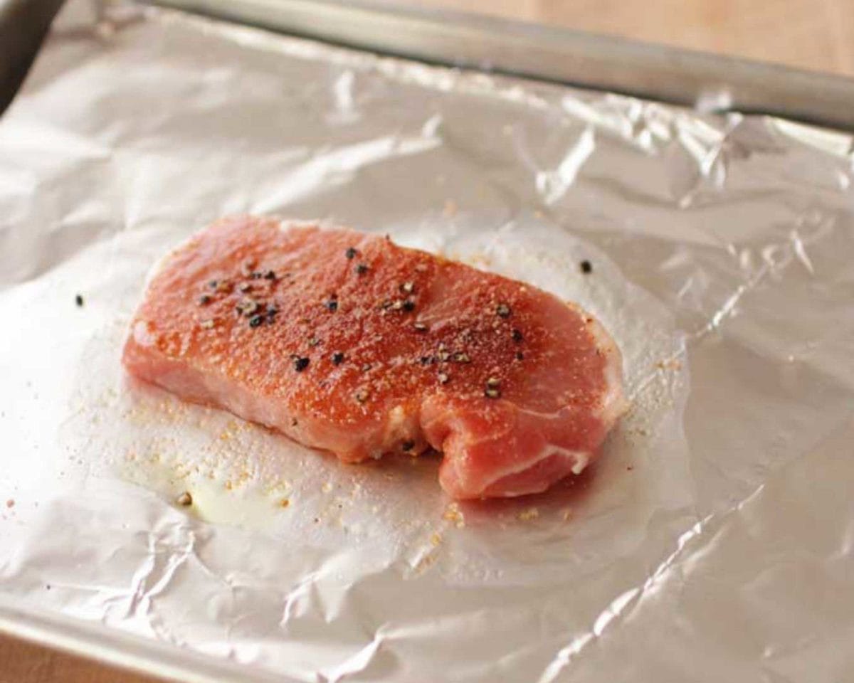 a raw pork chop on a foil lined rimmed baking sheet.