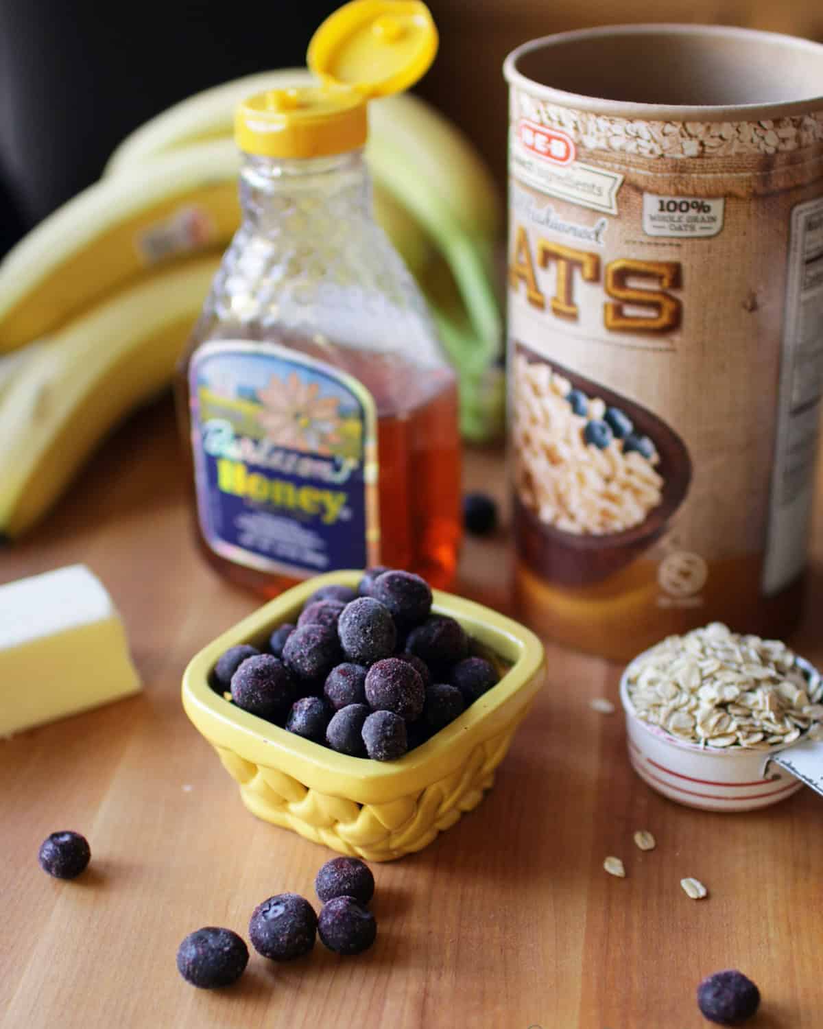 blueberries, bananas, oats, honey and butter on a brown cutting board.