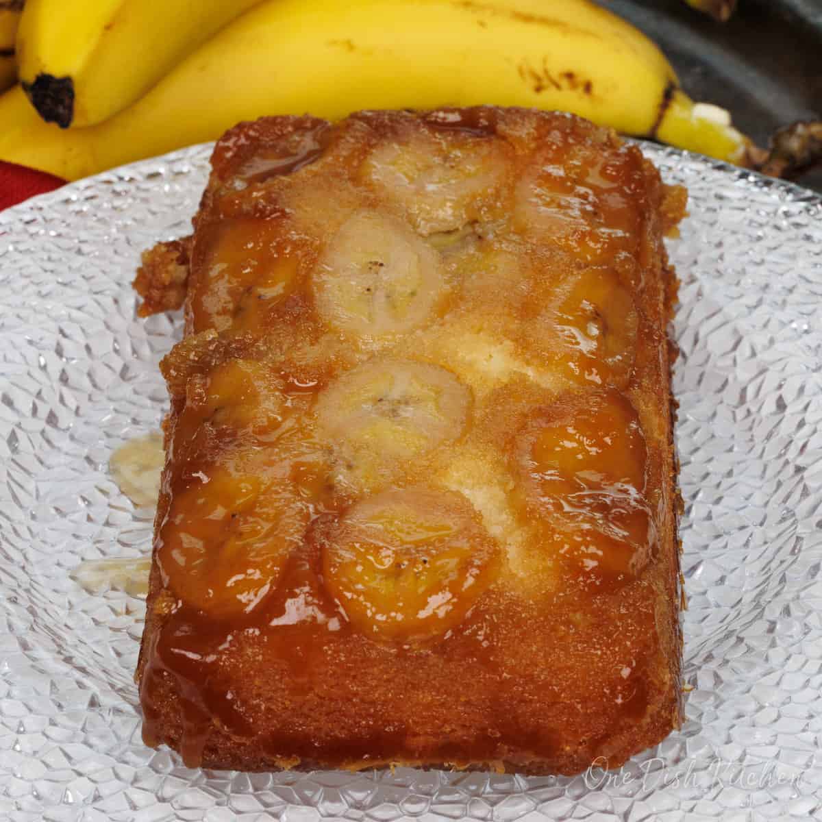 a mini caramelized banana upside down cake on a white plate next to two bananas.