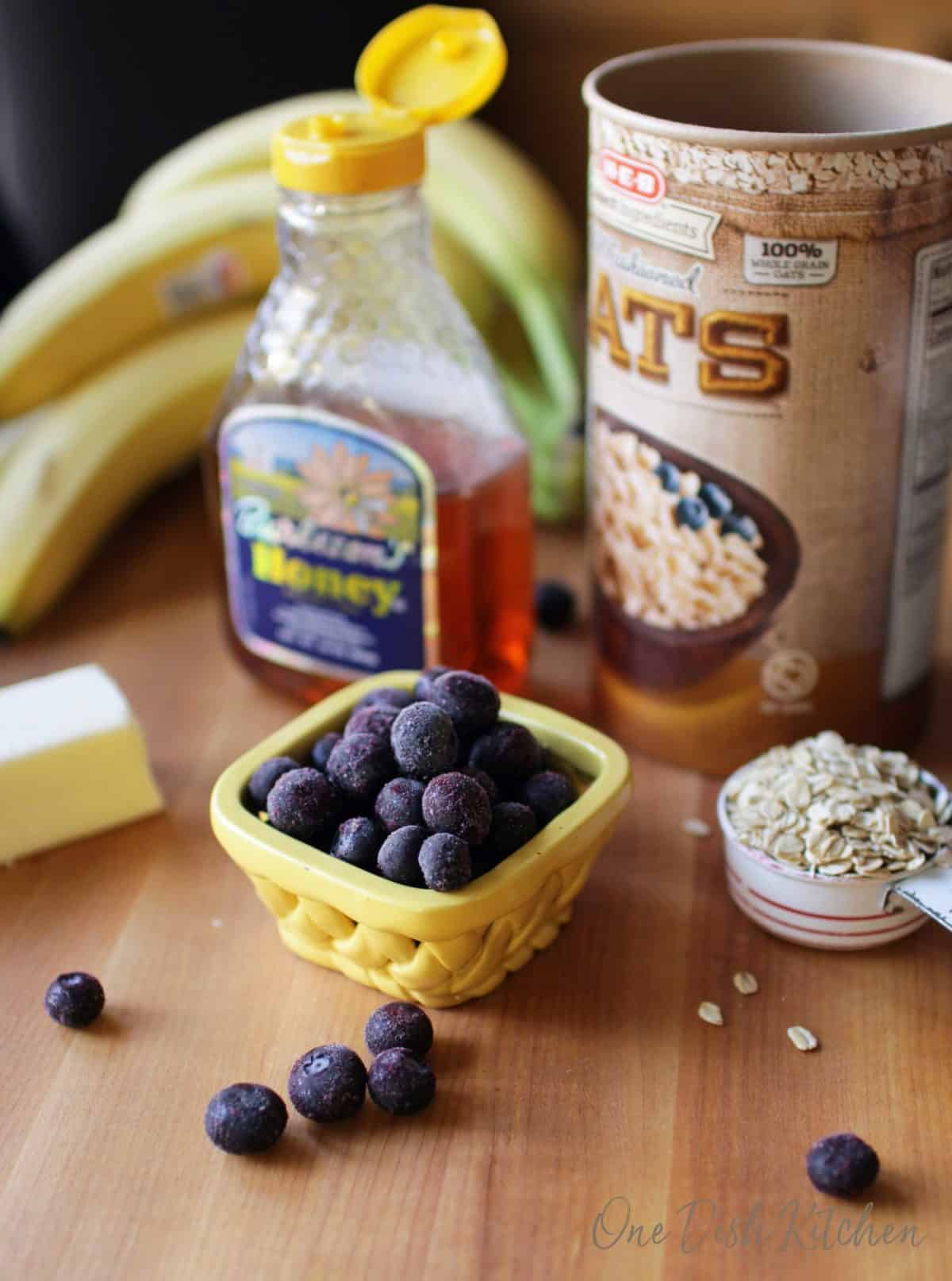 blueberries, bananas, oats, honey and butter on a brown cutting board.