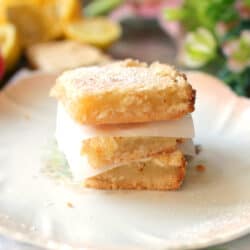 3 lemon bars on top of each other on a white plate next to a floral napkin