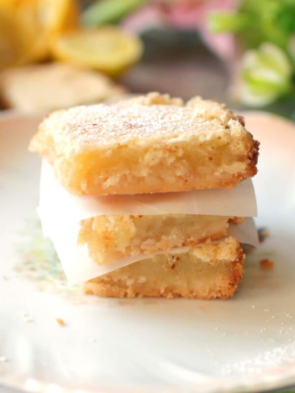 3 lemon bars on top of each other on a white plate next to a floral napkin